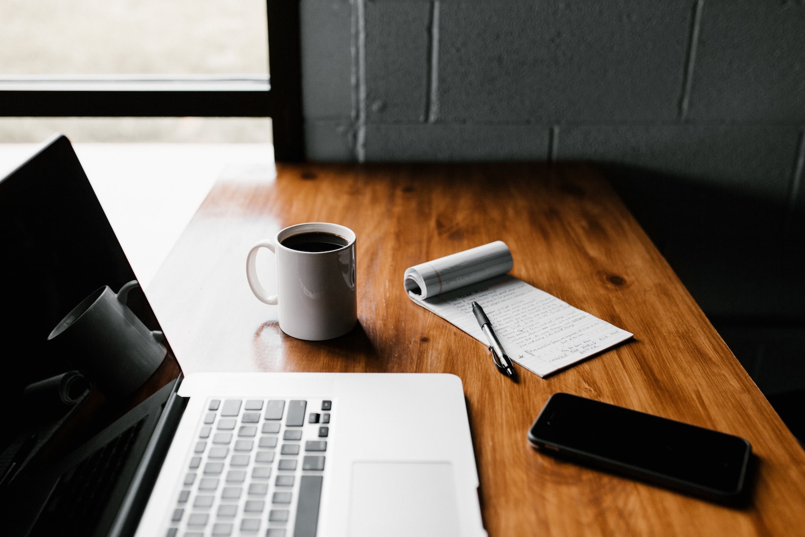 MacBook Pro, white ceramic mug and black smartphone on table